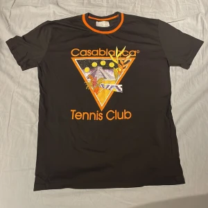 Svart t-shirt från Casablanca - Står storlek Xl men sitter som M!!! Snygg svart t-shirt från Casablanca med färgglatt tryck av 'Tennis Club' på både fram- och baksidan. Den har en cool orange och svart ribbad krage som ger en sportig look. 