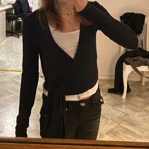 Svart omlottopp från Even&Odd - Trendig svart omlottopp från Even&Odd med långa ärmar och knytband i midjan. Väldigt eftertraktad. Är i helt nytt skick och har endast använts en gång. Säljer pga att den ej kommer till användning. Köpt för 210kr.