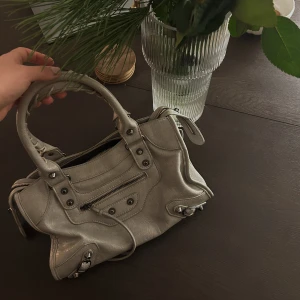 Grå väska - Snygg grå axelväska i skinn med dragkedja och stilrena detaljer. Perfekt för att bära med sig det nödvändigaste med stil.