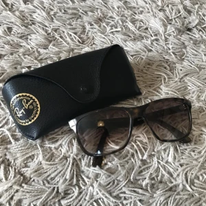 Svarta solglasögon från Ray-Ban - Snygga svarta solglasögon från Ray-Ban med fyrkantig form och mörka glas. Kommer med ett stilrent svart fodral. Perfekta för soliga dagar och ger ett klassiskt utseende. Obs Har skärpa