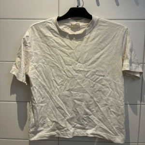 Vit t-shirt från Gina Tricot - Säljer en klassisk vit t-shirt från Gina Tricot. Den har en rund halsringning och korta ärmar, perfekt för en avslappnad stil. Tillverkad i ett mjukt material som känns skönt mot huden.