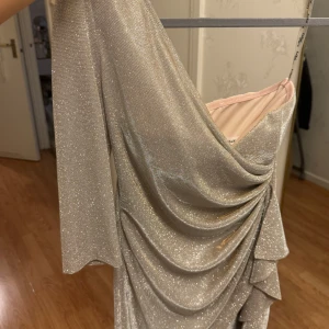 Glittrig klänning med drapering - Snygg glittrig klänning i silver med draperad design och trekvartsärm. Perfekt för en festlig kväll med sin eleganta och skimrande look.