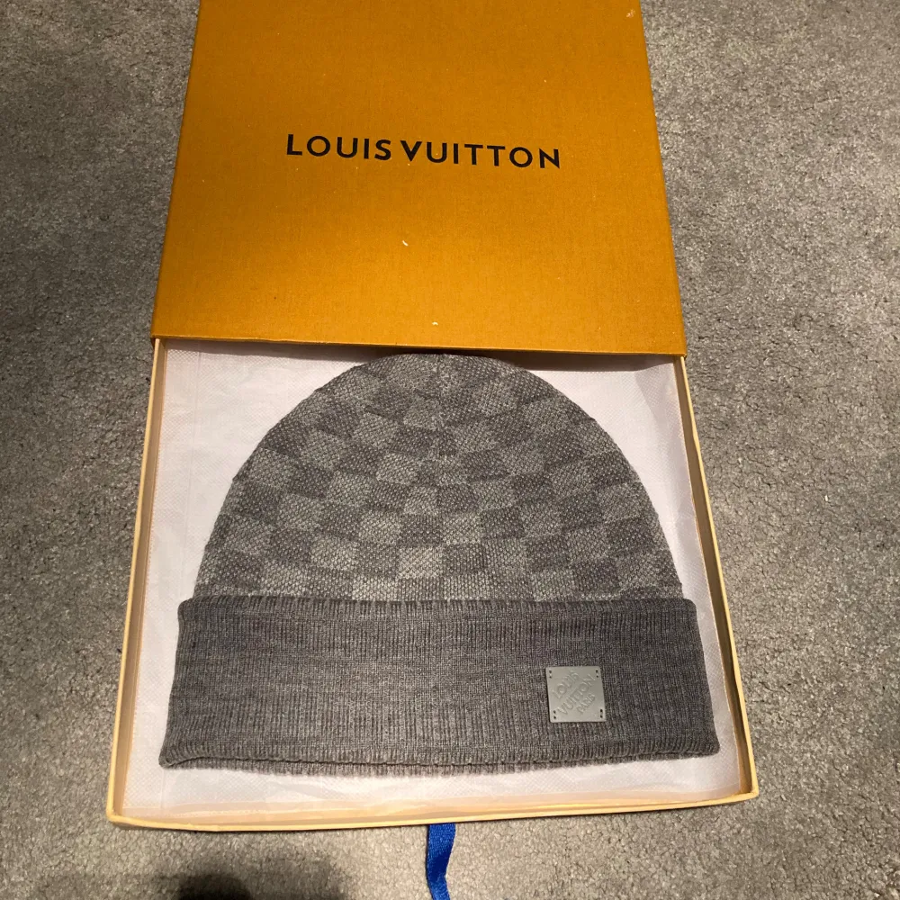 Snygg grå mössa från Louis Vuitton med klassiskt rutmönster. Mössan har en ribbad kant och en diskret logotypplatta framtill. Perfekt för att hålla stilen i kallare väder.. Asusteet.