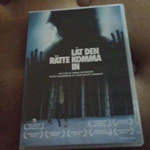 Låt den rätte komma in - DVD-film av Tomas Alfredson baserad på romanen av John Ajvide Lindqvist. Omslaget visar en mystisk siluett i en skogsmiljö med snö och träd. Filmen har fått flera utmärkelser och är en svensk produktion.