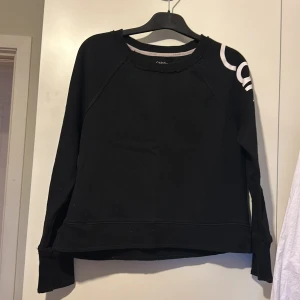 Svart tröja från Calvin Klein Performance - Snygg svart tröja från Calvin Klein Performance med vita detaljer och text längs ärmen. Perfekt för skolan. Tröjan har långa ärmar och en bekväm passform.