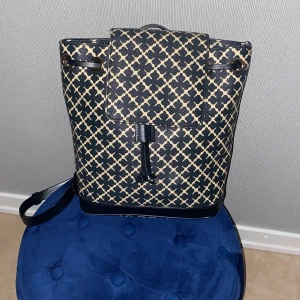Mönstrad ryggsäck med läderdetaljer - Säljer en by malene birger ryggsäck med ett unikt mönster i svart och beige. Väskan har läderdetaljer och en praktisk dragsko. Perfekt för att bära med sig det nödvändigaste med stil.