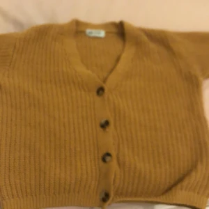 Beige stickad kofta från H&M - Mysig beige stickad kofta från H&M med knappar framtill. Perfekt för kyligare dagar med sin ribbade design och långa ärmar. En klassisk och bekväm tröja för barn.