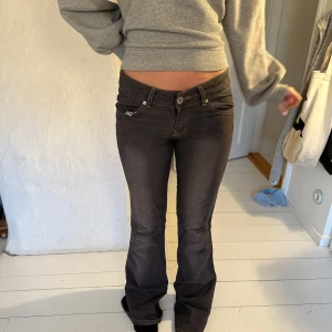 Mörkgrå bootcut jeans från Zinnia - Snygga mörkgrå bootcut jeans från Zinnia med låg midja. Perfekta för en avslappnad stil. Jeansen har klassisk femficksdesign och knappar framtill.