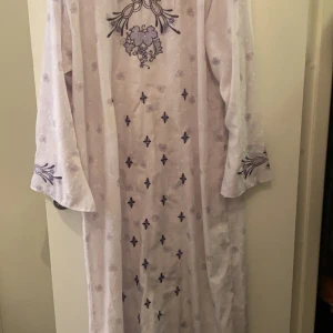 Vit långklänning med broderi - Elegant vit långklänning med lila broderade detaljer och blommönster. Klänningen har långa ärmar och ett vackert mönster framtill. Perfekt för speciella tillfällen. Helt oanvänd från Dubai dene XXL men kan få plats i XL och L om du gillar stora natt kläder 👍🏻
