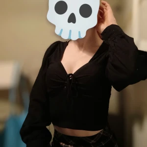 Svart croppad topp med knytning - Snygg svart croppad topp med knytning framtill. Toppen har långa ärmar och en djup v-ringning, perfekt för en trendig look.