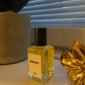 Vanillary parfym från Lush - En elegant flaska med Vanillary parfym från Lush. Parfymen har en varm och söt doft med inslag av vanilj. Flaskan är rektangulär med en svart kork och en enkel etikett.