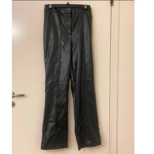 Svarta skinnbyxor - Snygga svarta skinnbyxor med hög midja och bootcut-stil. Perfekta för en trendig look med en modern twist. Byxorna har en slät yta och en stilren design. Helt oanvända läderbyxor som är utformat som kostymbyxor. Väldigt fina och sköna men tyvärr för långa för mig. Den är i storlek 38/M