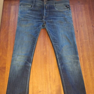 Blå jeans från Replay - Säljer ett par snygga blå jeans från Replay. Jeansen har en tapered passform och är tilverkade i denim. De har en klassisk femficksdesign med två bakfickor och tre framfickor. Jeansen har en knappgylf och är i övrigt i mycket bra skick.