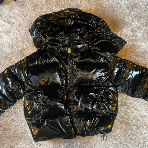 Calvin Klein Jeans svart glansig pufferjacka  - Säljer en svart glansig pufferjacka från Calvin Klein Jeans. Den är helt ny och aldrig använd . Köpte den för 3899kr. Jackan har en stor huva och dragkedja framtill. Perfekt för kyliga dagar med sin puffiga design som håller värmen.