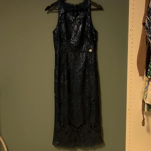 Mörkblå klänning från Chiara Forthi - Elegant mörkblå klänning från Chiara Forthi med vackert mönster och paljettdetaljer. Klänningen är ärmlös och har en figurnära passform som ger en stilren siluett. Perfekt för speciella tillfällen.