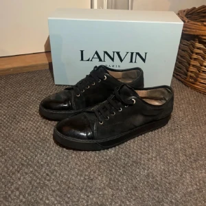  Lanvin - Snygga svarta sneakers från Lanvin med snörning och en stilren design. Skorna har en blank tå och är tillverkade i skinn, vilket ger dem en lyxig känsla. Perfekta för en stilmedveten look.
