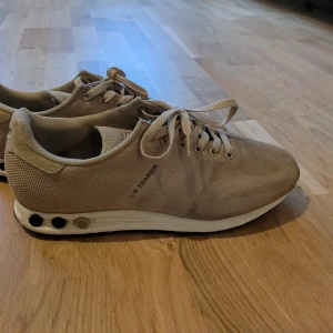 Beige sneakers från Adidas - Snygga beige sneakers från Adidas med snörning och en stilren design. Skorna har en vit sula med svarta detaljer och är perfekta för en avslappnad stil.