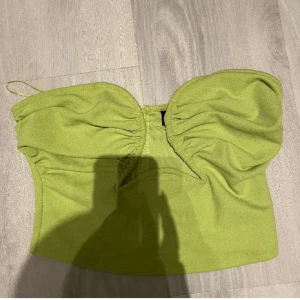 Grön tubtopp från Gina Tricot - Snygg grön tubtopp från Gina Tricot med fin urringning . Perfekt för en somrig fest look. Toppen har inga axelband och har en tight passform.