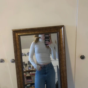 Vit ribbad polotröja - Säljer en stilren vit ribbad polotröja med långa ärmar. Tröjan har en tight passform och är perfekt för kyligare dagar. Den höga kragen ger en klassisk look.