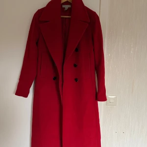 Röd kappa från H&M - Snygg röd kappa från H&M med klassisk design och knappar framtill. Perfekt för att ge en färgklick till din outfit. Kappan är i ett ullmix-material. Nypris 1500:- 