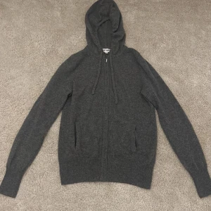 Grå hoodie från Soft Goat - Säljer en stilren grå hoodie från Soft Goat i kashmir. Tröjan har en dragkedja framtill och en praktisk huva. Perfekt för kyliga dagar med sin mjuka och bekväma passform. Två fickor framtill för extra funktionalitet.