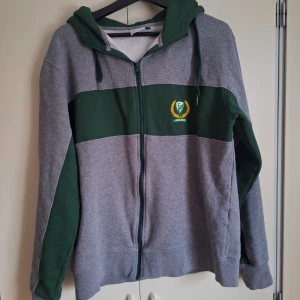 FBK hoodie  - Säljer en grå och grön hoodie med dragkedja från SHL. Tröjan har en grön huva och ett FBK emblem på bröstet! 🤍💚