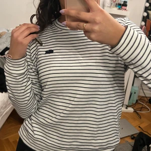 Randig tröja från Lacoste - Säljer en stilren vit och svart randig tröja från Lacoste. Tröjan har långa ärmar och en klassisk rund halsringning. Perfekt för en avslappnad och trendig look. 🖤🤍