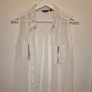 Snygg vit ärmlös blus från Lindex i ett transparent material. Den är dekorerad med kedjedetaljer på fickorna, liten defekt på den ena fickan därav lågt pris.