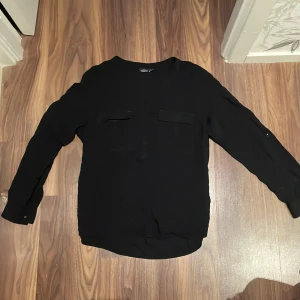 Svart blus med fickor  -  Säljer en svart blus från Kappahl i storlek M med två dekorativa fickor framtill och knappar upptill samt på ärmarna. ⭐️ Blusen är tillverkad i ett tunt och genomskinligt material. 