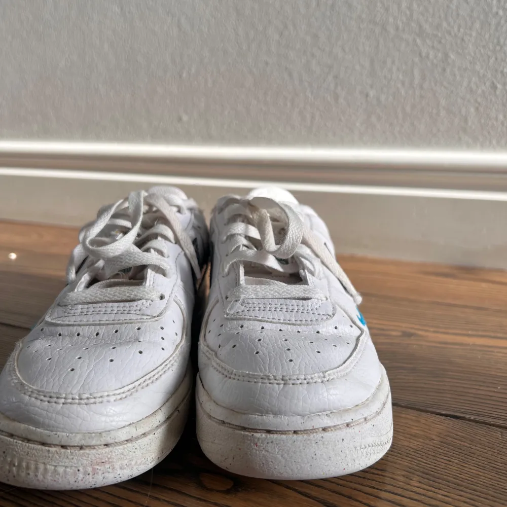 Snygga vita Nike Air sneakers med blå swoosh och detaljer. Skorna har klassisk snörning och perforeringar på ovansidan för ventilation. Perfekta för en sportig look.. Kengät.