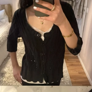 Svart kofta med knappar - Säljer en svart kofta med knappar framtill. Koftan har trekvartsärmar och ett fint stickat mönster. Perfekt för lager-på-lager-stil och passar till många olika outfits. S/M