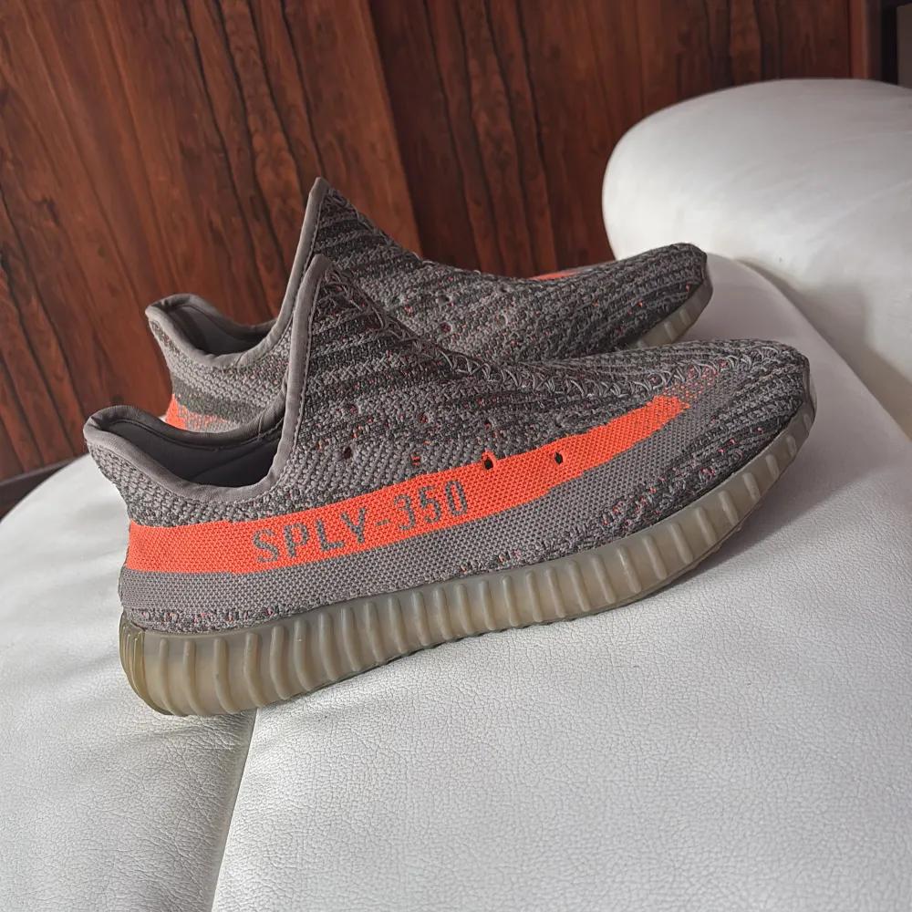 Säljer ett par Adidas Yeezy Boost 350 V2 i grått med orange detaljer. Skorna har den ikoniska SPLY-350 texten på sidan och en randig design. De har en bekväm och dämpande sula som är perfekt för vardagsbruk. ( KVITTO FINNS I BILD). Kengät.