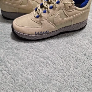 Beige och blå Nike sneakers - Snygga beige sneakers från Nike med blå detaljer och snörning. Skorna har en unik sula med blå och orange mönster. Perfekta för en sportig look. Och nästan helt nya, använda 2 gånger. Pris diskuteras vid snabb affär