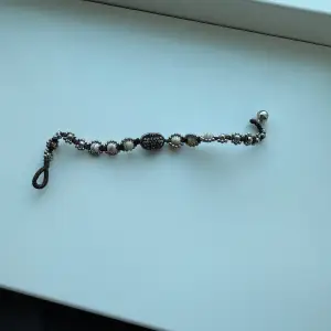 Charmigt armband med vita pärlor och en central metallisk detalj. Armbandet har en elastisk slinga för enkel påtagning och en liten metallkula som avslutning. Perfekt för att ge en elegant touch till din outfit.
