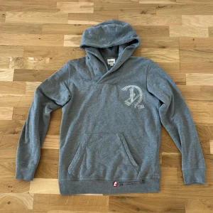 Grå hoodie från Diesel - Säljer en stilren grå hoodie från Diesel med en stor D-logga och årtalet 1978 tryckt på bröstet. Tröjan har en bekväm passform med långa ärmar och en praktisk känguruficka framtill. Perfekt för en avslappnad stil.
