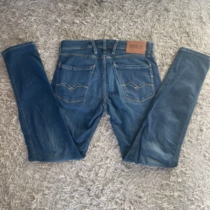 Blå jeans från Replay - Snygga blå jeans från Replay med klassisk femficksdesign och snygga sömmar på bakfickorna. De har en knappgylf och är perfekta för en avslappnad stil. Märkeslappen i läder på baksidan ger en extra touch.