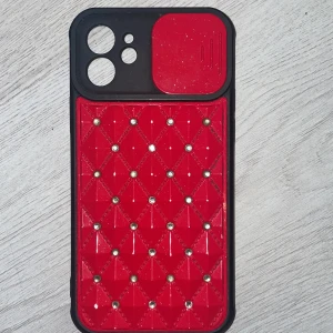 Röd och svart mobilskal med glittriga detaljer till iphone 12 - Snyggt mobilskal i rött och svart med quiltad design och glittriga detaljer✨ Skalet har en robust känsla och skyddar din telefon samtidigt som det ger en stilren look. Perfekt för att ge din mobil en personlig touch. Den är inte använd alls mycket och har även ett lock så att man kan täcka kameran. Jag ansvarar ej för postens slarv🤝 köpte för ca 100kr