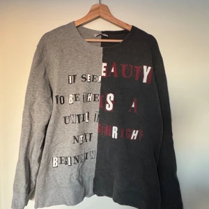 Grå och mörkgrå tröja från Valentino - Säljer en unik tröja från Valentino i två nyanser av grått med texttryck på framsidan. Tröjan har en delad design med långärmade ärmar och rund hals. Perfekt för en stilren och modern look. Mycket bra skick - storlek M.