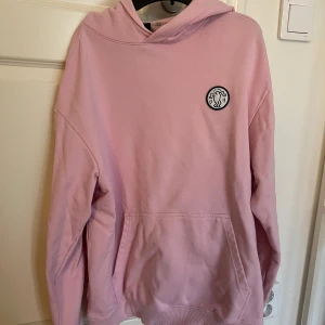 Rosa hoodie från H&M x Keith Haring - Säljer en rosa hoodie från H&M i samarbete med Keith Haring. Tröjan har en stor ficka fram och ett ikoniskt Keith Haring-motiv på ryggen. Perfekt för en avslappnad stil med en konstnärlig touch.