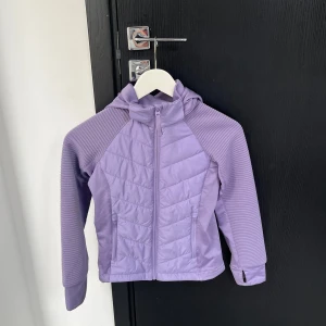 Lila jacka med huva - Snygg lila jacka med dragkedja och huva. Jackan har quiltade detaljer och långa ärmar. Perfekt för vår och höst.