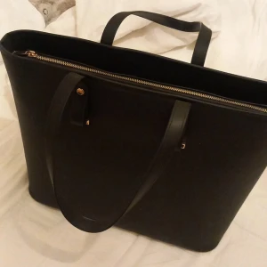 Svart axelväska med dragkedja - Jag säljer en stor svart handväska från hm med guldig dragkedja och guldiga detaljer. Väskan har jätte praktiska fack på insidan, det var svårt att få med det tydligt på bild men det finns där!💗Jag säljer pågrund utav att den inte kommer till användning. (Jag kan gå upp och ner i pris) Skriv vid intresse av att köpa!💗💗