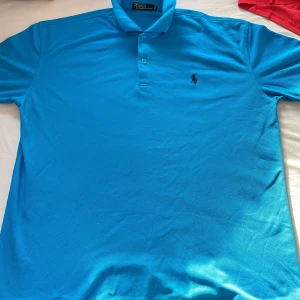 Blå pikétröja från Ralph Lauren - Säljer en snygg blå pikétröja från Ralph Lauren med klassisk krage och knappar framtill. Tröjan har en broderad logotyp på bröstet och är perfekt för en stilren look. Passar både till vardags och mer uppklädda tillfällen.