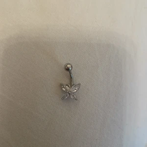 Navelpiercing med fjärilsdesign - Elegant navelpiercing i silverfärg med en glittrande fjärilsdesign. Perfekt för att ge en extra touch av stil och glamour.