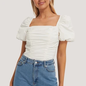 Vit topp - Säljer en  vit blus från Chloé B x NA-KD med puffiga korta ärmar och rynkade detaljer framtill. Endast använd 1 gång.