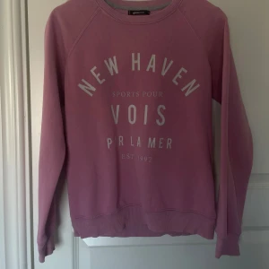 Rosa sweatshirt från Gina Tricot - Säljer en rosa sweatshirt från Gina Tricot med texten 'New Haven' tryckt på framsidan. Tröjan har långa ärmar och ribbade muddar vid ärmslut och nederkant. Perfekt för en avslappnad stil.