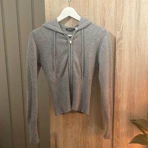 Grå hoodie från Gina Tricot - Säljer en stilren grå hoodie från Gina Tricot i storlek S. Tröjan har en dragkedja framtill och en mysig huva med snören. Priset är diskuterbart. 