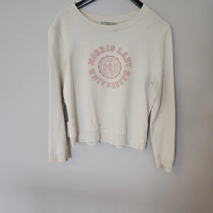 Vit tröja från Morris Lady - Säljer en vit tröja från Morris Lady med tryck i rosa på framsidan. Tröjan har långa ärmar och en rund halsringning. Perfekt för en avslappnad stil. Hör av dig vid intresse!
