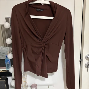 Brun långärmad topp med knutdetalj - Snygg brun långärmad topp i stl S med en elegant knutdetalj framtill. Toppen har en  v-ringning som man kan justera och är tillverkad i ett mjukt och stretchigt material. 🤎🤎🤎