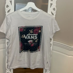 Vit t-shirt från Vans med blommigt tryck - Säljer en vit t-shirt från Vans med ett stort blommigt tryck och texten 'Off The Wall' på framsidan. T-shirten har korta ärmar och en klassisk rund halsringning. Perfekt för en avslappnad stil. 🌸