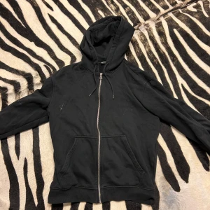 Svart hoodie från Weekday - Säljer en svart hoodie från Weekday i storlek S. Den har en dragkedja framtill och en klassisk huva med snören. Perfekt för en avslappnad stil och passar till de flesta tillfällen. Fortfarande i bra skick!